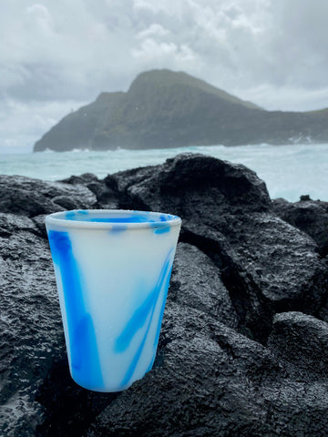 Reusable Silicone Ocean Cup Sitting on a Rock with the Ocean in the Background 