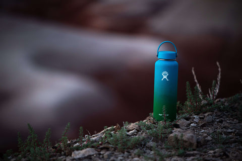 A stainless steal water bottle sitting on the ground with nature as background