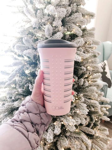 A reusable sustainable silucone Gosili cup being held by a women's hand in front of a white Christmas tree