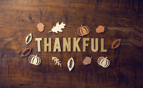 Laying on a wooden table is a cut out of foam paper that reads "thankful" in sparkly gold color along with Thanksgiving related shapes. 