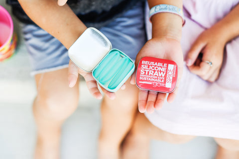 Two kids holding a travel tin with a reusable silicone straw in it