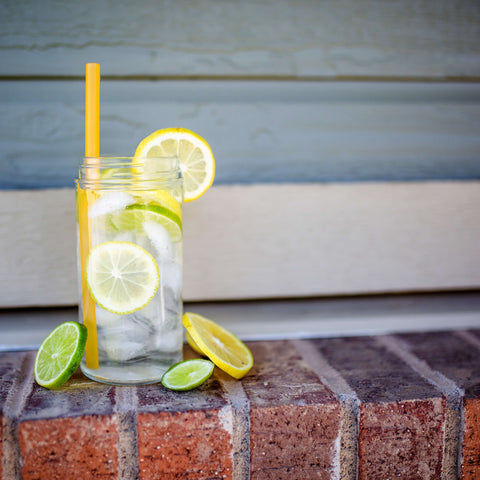 A glass of water with limes and lemons with a yellow reusable silicone straw