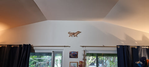 A dachshund (sausage dog) shaped clock made from bronze metal, hanging above a doorway. There are black curtains to the left and right hand side.