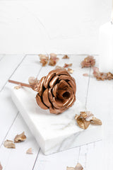 A rose made entirely from copper, displayed on a marble slab and entirely white background.