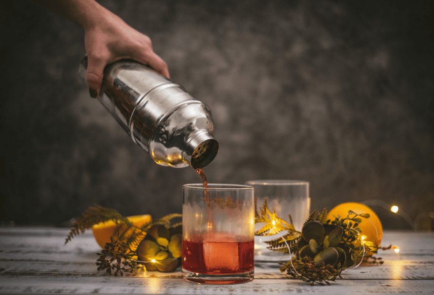 A person pouring a non-alcoholic Negroni into a glass