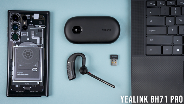 Image of yealink BH71 pro earpiece, charge case, and USB adapter on desk top next to mobile phone and computer keyboard 