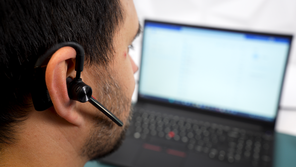 Man sitting at a desk, facing a computer screen wearing a Yealink BH71 earpiece headset