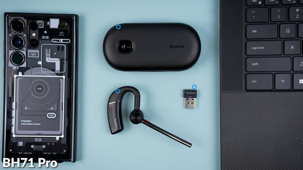 Yealink BH71 Pro earpiece, case and USB adapter on desk top next to computer and mobile phone