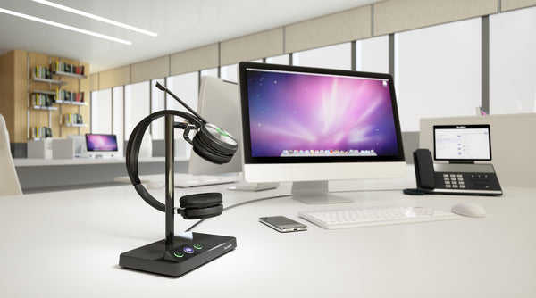 Yealink WH62 wireless headset docked on stand resting on desktop in an office setting