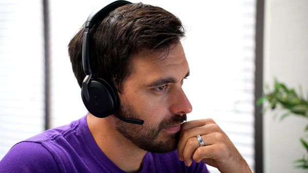 man sitting at an office desk wearing a Jabra Evolve2 65 Flex headset with the microphone boom arm dropped down.