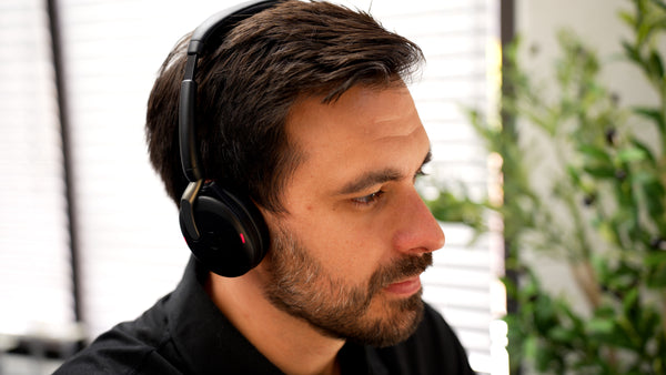 Side view of a man sitting at an office desk wearing a Jabra Evolve2 65 Flex headset with the microphone boom arm tucked out of sight