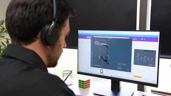 Man sitting at an office desk in front of a computer wearing a Jabra Evolve2 65 Flex headset