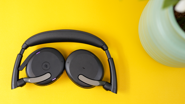 Jabra Evolve2 65 Flex headset folded in half on yellow desk top with a plant partially in view on the right