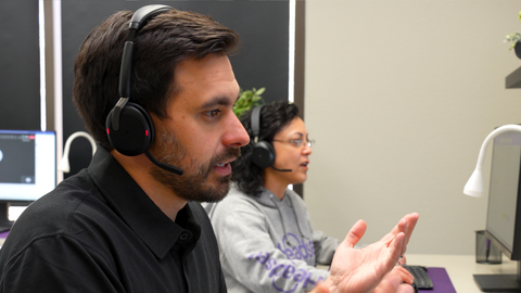 man on headset in office in foreground on a call, and a woman on a call in the background