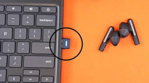 close up view of two Poly Voyager Free 60 earbuds on desktop next to computer with USB adapter inserted in computer and a drawn circle around the adapter