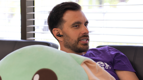 man sitting on sofa in office wearing Poly Voyager Free 60 earbuds while on a call