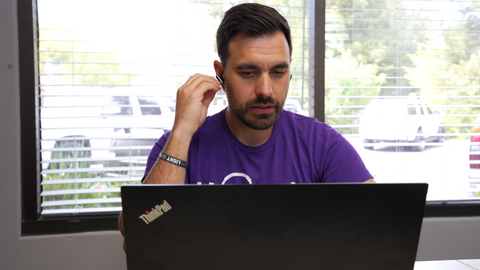 man sitting at desk in front of laptop looking at the screen and inserting a Poly Voyager Free 60 earbud into his ear