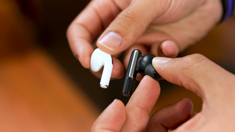 man holding Apple  AirPod earbud and Poly Voyager Free 60 earbud side by side