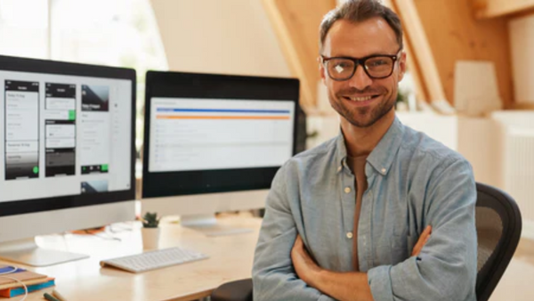 IT Man behind desk, in front of monitors smiling