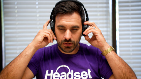 man sitting at a desk wearing a Headset Advisor T-shirt, trying on a Jabra Evolve2 65 Flex bluetooth headset