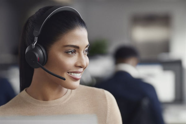 side view of a woman wearing a Jabra Evolve2 65 mono headset smiling while working in an office setting