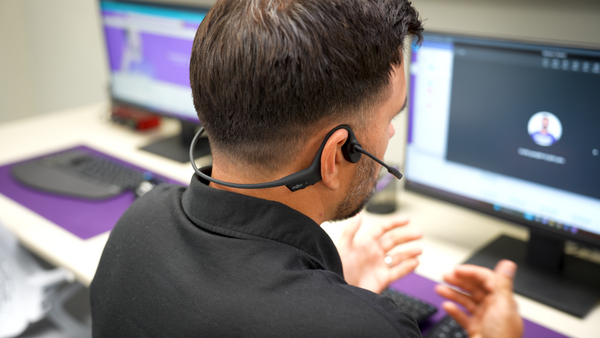 Man sitting at an office desk facing a computer screen while wearing an Opencomm2 UC headset