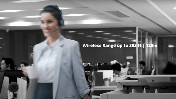 professionally dressed woman walking across an open office area wearing a Yealink  WH62 wireless headset