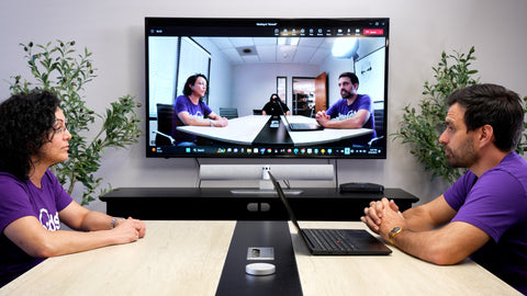 Man and woman sitting across a meeting table in an office while on a video call