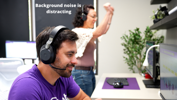 man sitting at desk in the foreground wearing a headset, woman wearing headset in background standing up making noise