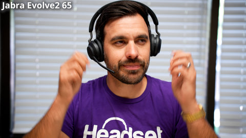 man sitting at desk wearing a Headset Advisor Tshirt putting on a Jabra Evolve2 65 bluetooth wireless headset