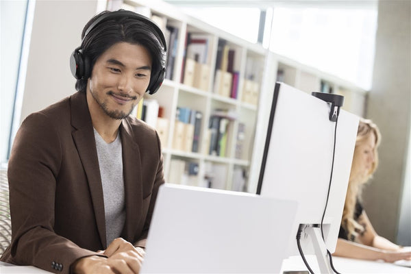 Man sitting at desk in front of a computer monitor wearing a Jabra Evolve2 75 headset, smiling while sitting in close proximity to a coworker to his left