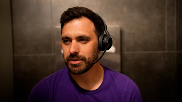 Man sitting on the toilet in a bathroom wearing a Jabra Evolve2 55, and on a call