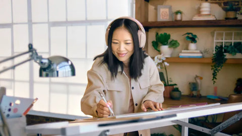 Woman working at drafting table wearing white colored Zone Vibe 100 headset
