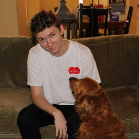 a man in a plain white shirt sitting on a couch, petting a golden retriever