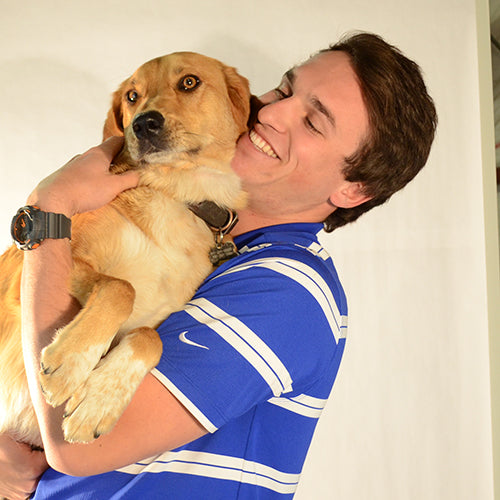 A smiling man in a blue striped shirt holding a golden retriever in his arms