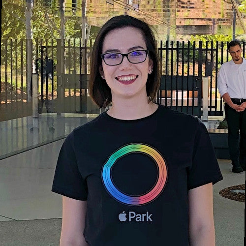 a woman with glasses and a rainbow circle on her black shirt smiling at the camera