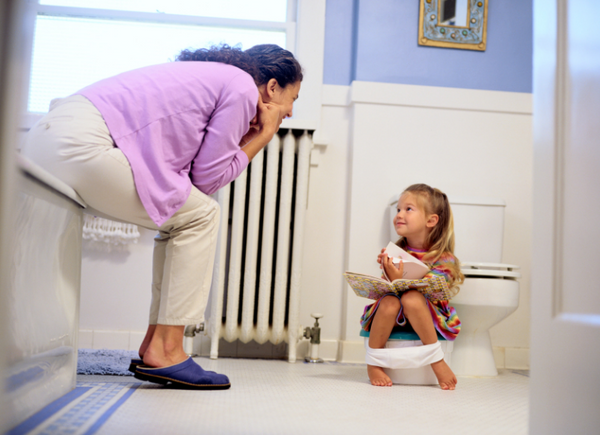 Girl reading a book on a potty chair with her mom