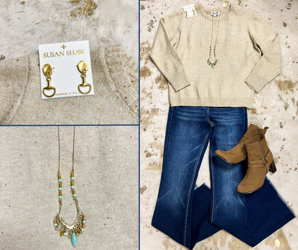 Flat lay of light beige embellished sweater, dark wash flare jeans, tan boot with heel, gold drop earrings, and gold and sea green beaded necklace.