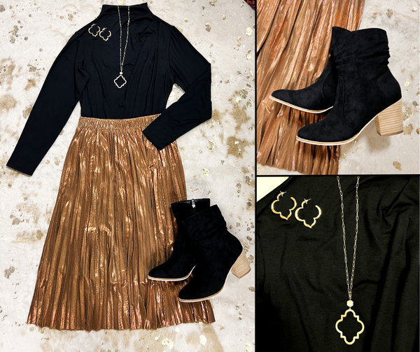 Flat lay of bronze metallic midi skirt, black mock neck top, black suede pointed toe boots with heel, and clover shaped earrings and pendant necklace.