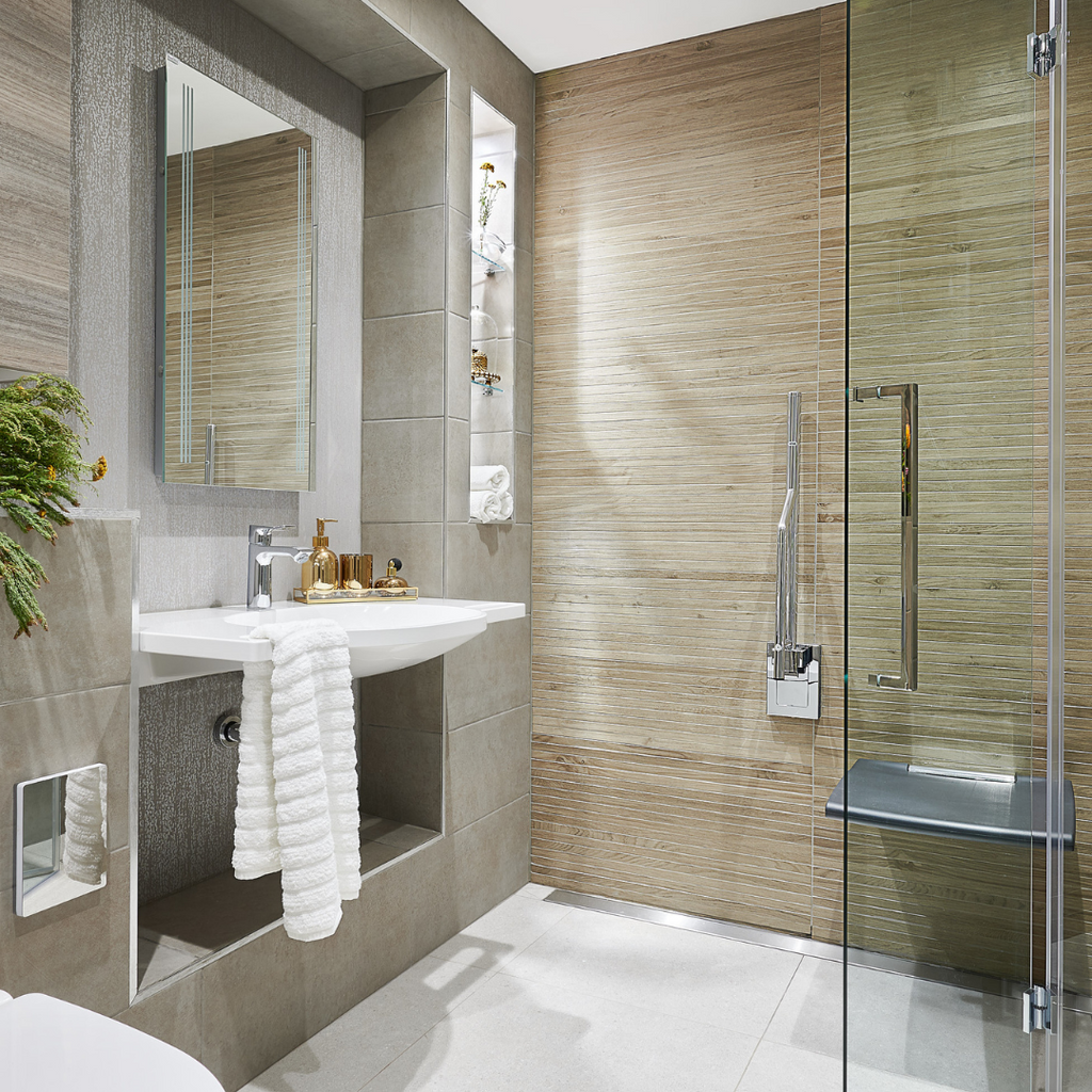  A sand coloured accessible wetroom with illuminated mirror and storage niche above a wall hung sink, glass shower screen and folding shower seat