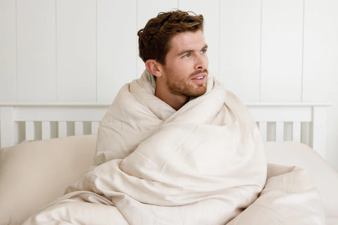 man sitting on a bed with a duvet cover wrapped around him