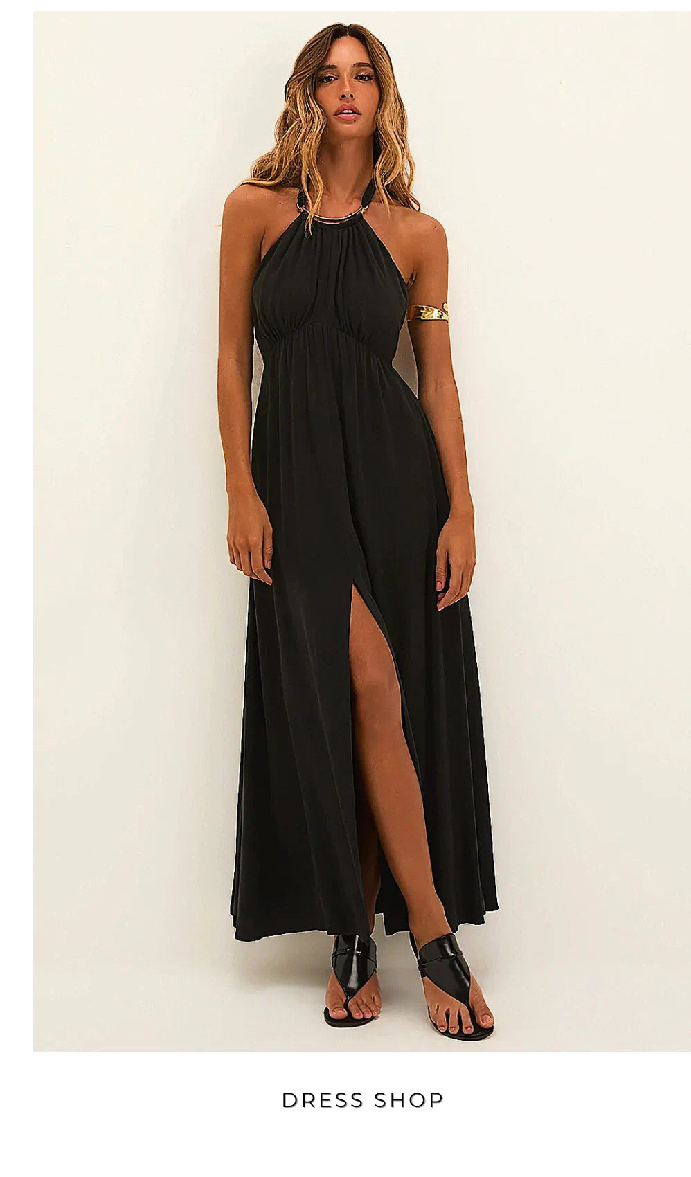 Model in a black halter maxi dress with front slit, styled with gold arm cuff and black sandals — Dress Shop edit.