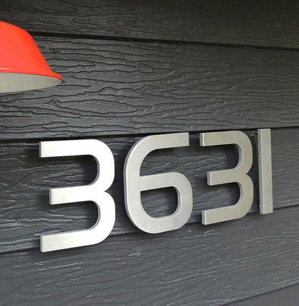 Modern House Numbers 6" South Beach Numbers in Brushed Aluminum installed on a home with dark gray shiplap siding, white painted trim, with a red wall mounted light fixture.