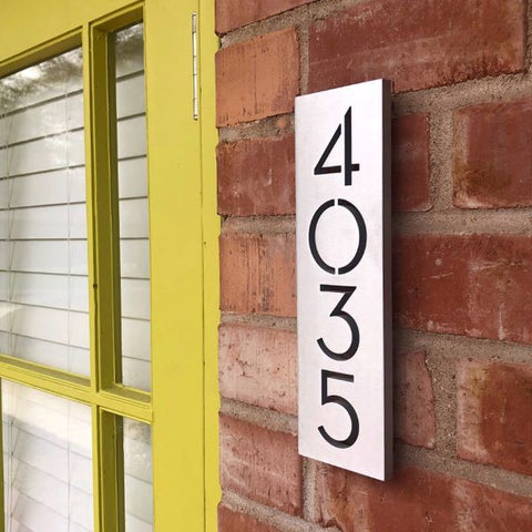 Modern vertical plaque, sign '4035' in brushed aluminum finish. Exterior brick wall with yellow framed door. 