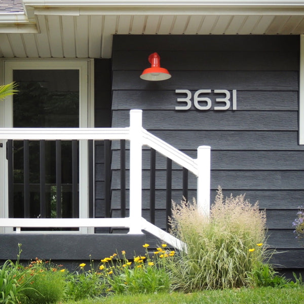 Modern House Numbers 6" South Beach Numbers in Brushed Aluminum installed on a home with dark gray shiplap siding, white painted trim, with a red wall mounted light fixture.. 