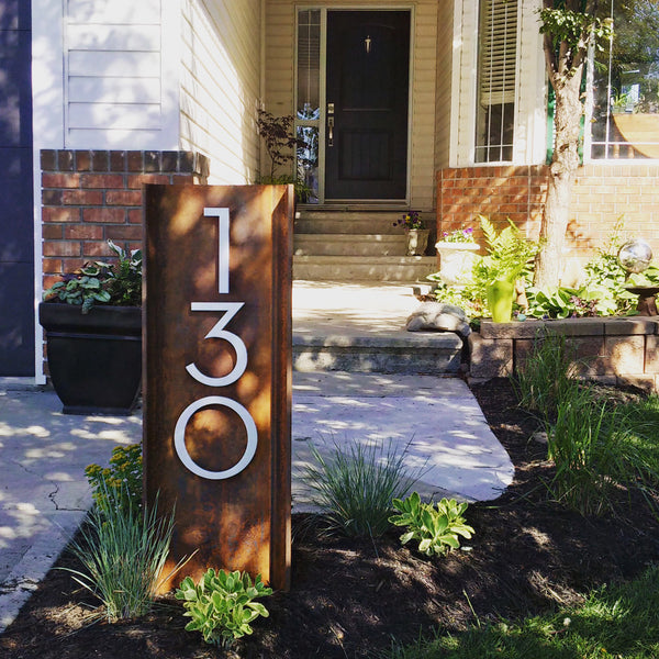 Modern House Numbers '130' Palm Springs font, vertical orientation, Brushed Aluminum finish installed on a free standing section of a rusted steel beam. Set into the lawn near the driveway.