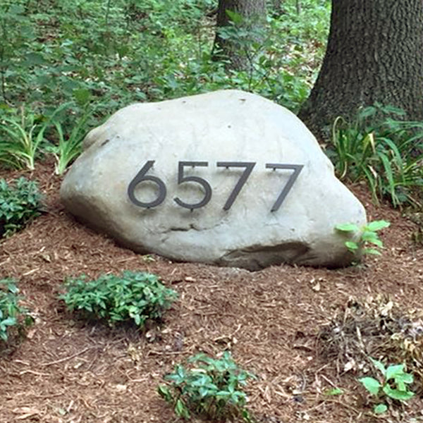 Modern House Numbers '6577' Palm Springs font, Dark Bronze finish, installed on a light gray boulder in the landscape.