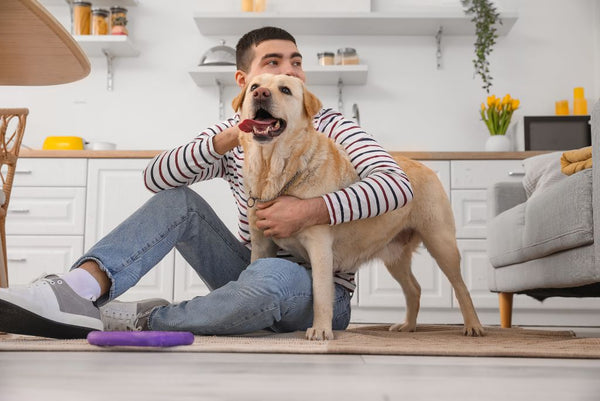 Man sitting on kitchen floor, hugging his dog