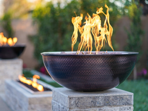 A Copper Fire Bowl With Flames On Top Of Pedestal