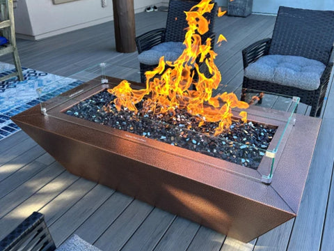 A Rectangle Copper Fire Pit With Fire Glass and Glass Wind Guard Sitting On A Deck